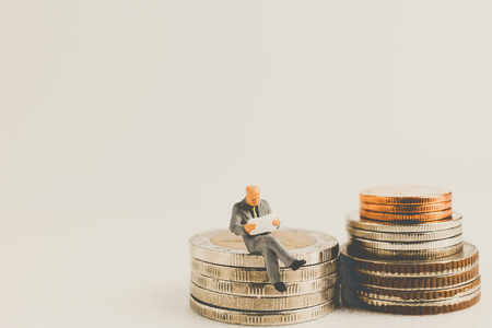 Miniature people business concept sitting on coins with a space for textの写真素材