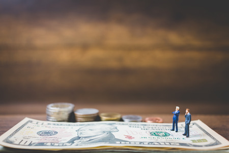 Miniature people businessman on money on wooden backgroundの写真素材