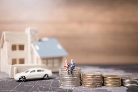 Miniature people sitting with coins money with home. Investment and growth in business concept.の写真素材