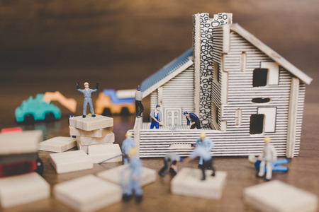 Miniature people worker repairing are repairing house on wooden background.