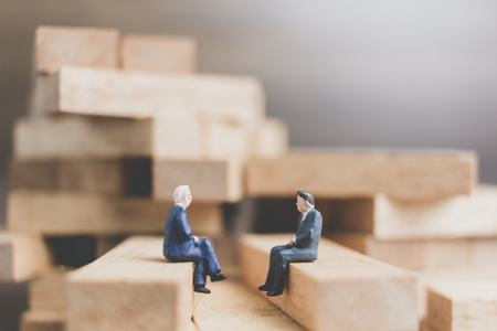 Miniature people : Business People sitting on wood block with wooden backgroundの写真素材