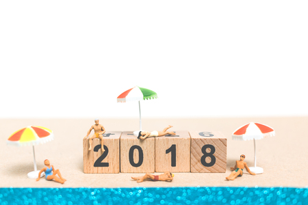 Miniature people wearing swimsuit relaxing on the beach With Wooden block number 2018