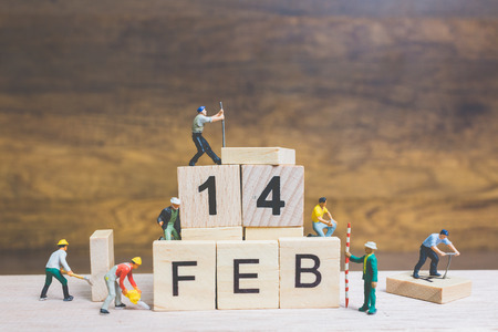 Miniature people : Worker team building word " 14 FEB " on wooden block with wooden background , Valentine's day conceptの写真素材