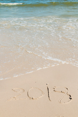 Handwritten " 2018 " on a sand of beach with wave  backgroundの写真素材