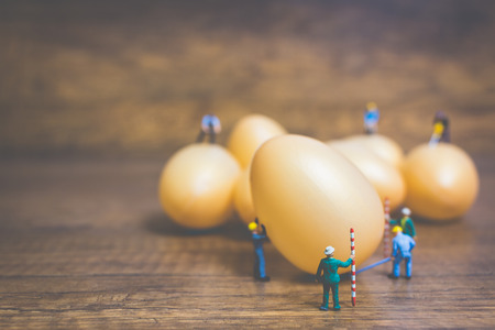 Miniature people work at Easter-eggs for Easter day on wooden backgroundの写真素材