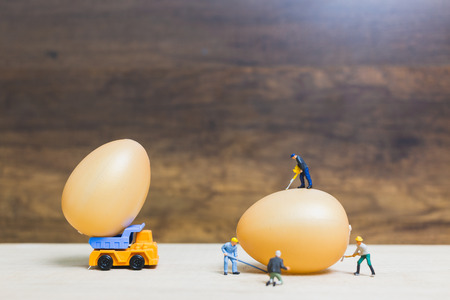 Miniature people work at Easter-eggs for Easter day on wooden backgroundの写真素材