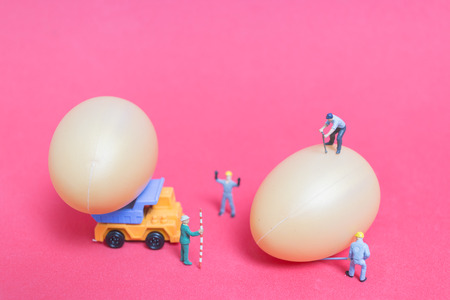 Miniature people work at Easter-eggs for Easter day on pink backgroundの写真素材