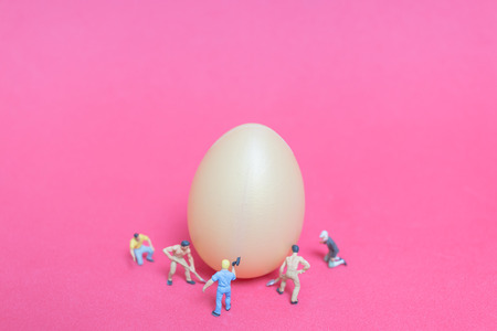 Miniature people work at Easter-eggs for Easter day on pink backgroundの写真素材