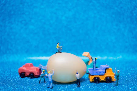 Miniature people work at Easter-eggs for Easter day on blue glitter backgroundの写真素材