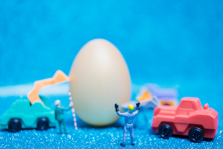 Miniature people work at Easter-eggs for Easter day on blue glitter backgroundの写真素材