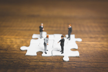Miniature people: Businessman standing on jigsaw with wooden background : Business concept.の写真素材