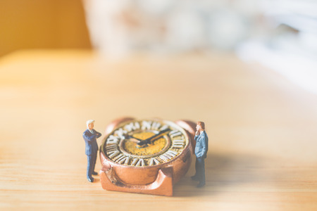 Miniature people: Businessman standing with Ancient clock on wooden backgroundの写真素材
