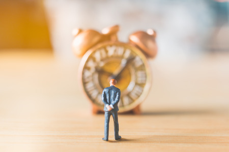 Miniature people: Businessman standing with Ancient clock on wooden backgroundの写真素材