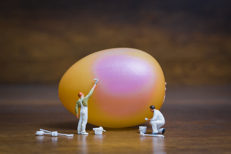 Miniature people :Painter is painting Easter-eggs for Easter day on wooden backgroundの写真素材
