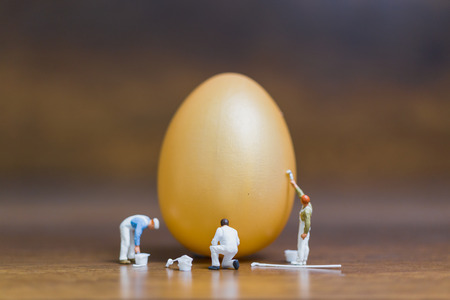 Miniature people :Painter is painting Easter-eggs for Easter day on wooden backgroundの写真素材