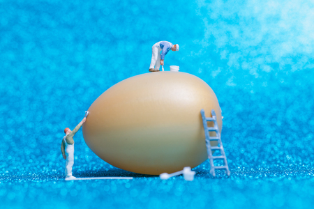 Miniature people :Painter is painting Easter-eggs for Easter day on blue glitter  backgroundの写真素材