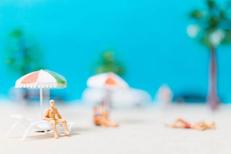 Miniature people wearing swimsuit relaxing on the beach with blue backgroundの写真素材