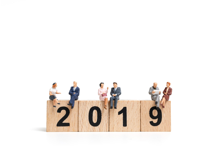 Miniature people sitting on wooden block number 2019. on white background