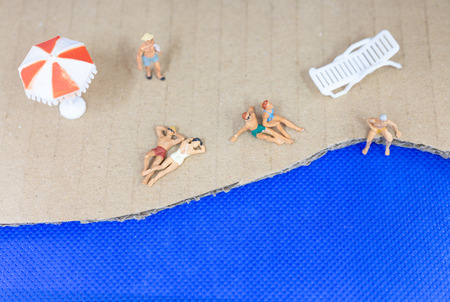 Miniature people wearing swimsuit relaxing on the beach with blue backgroundの写真素材