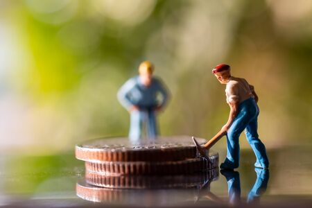 Miniature people worker holding tool on coins with green bokeh background , Construction conceptの写真素材