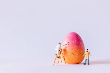 Miniature people painting Easter-eggs for Easter day on white background
