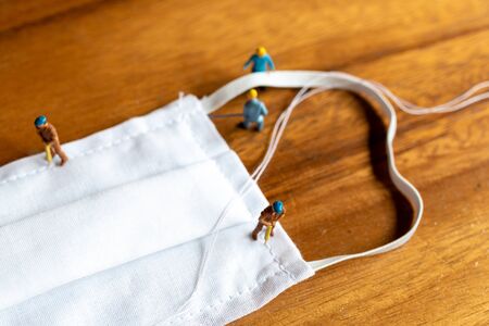 Miniature people : worker team making a homemade mask from white fabric on wood table backgroud
