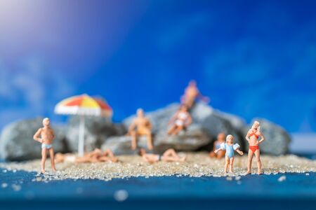 Miniature people wearing swimsuit relaxing on the beach with blue background , Summer time conceptの写真素材