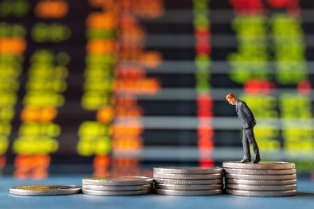Miniature people , Businessman standing on stack of  Coins with graph display backgroundの写真素材