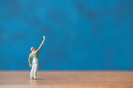 Miniature people holding brush in front of a blue wall backgroundの写真素材