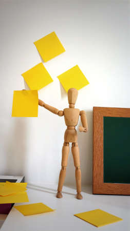 Wooden Human With Blank Yellow Paper on Wall, Empty Space For Text, Funny Idea.