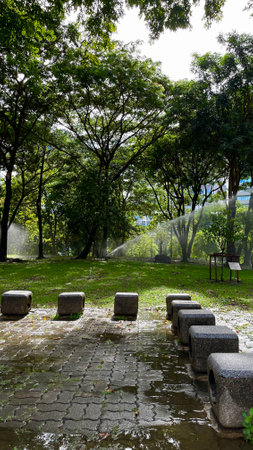 Park bench and water sprinkler in the public park, Thailand.の写真素材