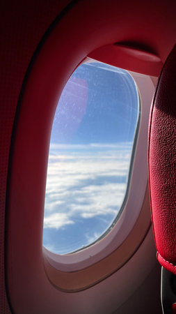 Airplane window view of clouds and blue sky from porthole