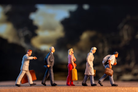Miniature figures carrying luggage walk against a somber backdrop, symbolizing displacement and the...