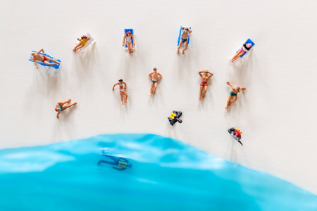 Miniature people relax on sun loungers, enjoying the sunshine, while others swim in a vibrant blue ocean, Perfect for concepts of summerの写真素材
