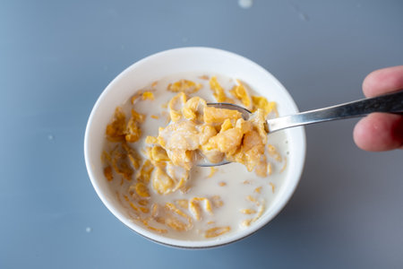 A spoon lifting a portion of crispy cornflakes soaked in milk from a bowl. A delicious and classic...