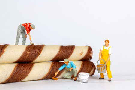 Tiny figurines of painters appear to be painting chocolate stripes on rolled wafer cookies, creating...