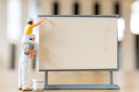 Miniature figurine painting a blank sign or board. Ideal for concepts like creativity, advertising, message spaceの写真素材