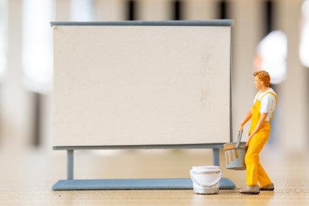 Miniature figurine painting a blank sign or board. Ideal for concepts like creativity, advertising, message spaceの写真素材