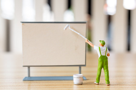 Miniature figurine painting a blank sign or board. Ideal for concepts like creativity, advertising, message spaceの写真素材