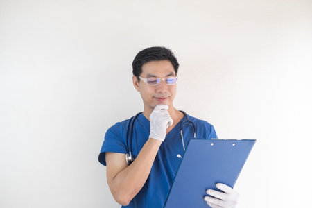 Asian male healthcare worker wearing blue scrubs holding a blue clipboard and looking at it thoughtfully.の写真素材