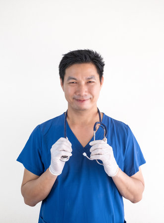 Portrait of a confident Asian male nurse wearing blue medical scrubs standing against a white wall backgroundの写真素材