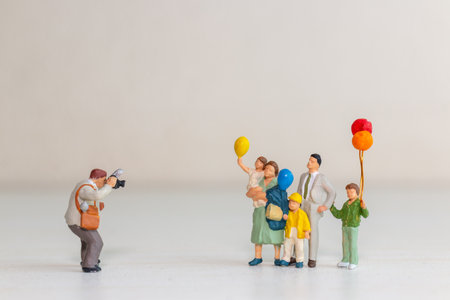 Adorable conceptual image featuring miniature figurines of a family posing for a photograph while holding colorful balloonsの写真素材