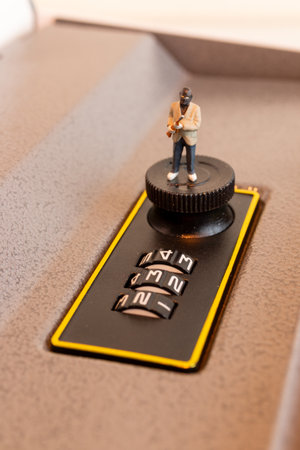 Creative concept photo featuring a miniature figurine of a masked thief attempting to crack the code on a combination safe lockの写真素材