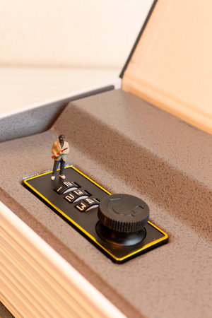 Creative concept photo featuring a miniature figurine of a masked thief attempting to crack the code on a combination safe lockの写真素材