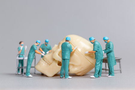 Tiny toy doctors in scrubs perform a delicate and precise surgery on a large human skull model,...