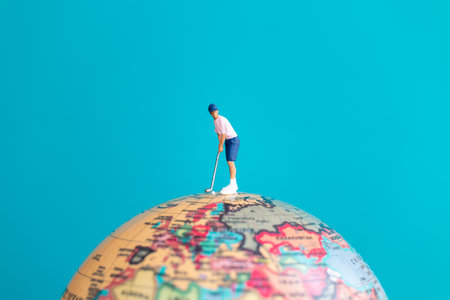 A miniature figure of a golfer playing on top of a globe, symbolizing global sport, travel, and imagination.の写真素材