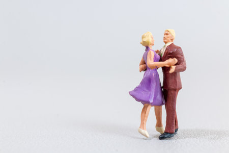 Small figurines of dancing couples in colorful outfits on a light grey textured surfaceの写真素材