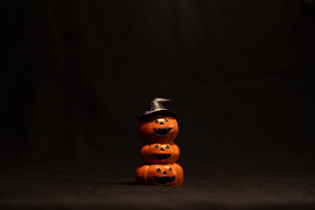Stacked pumpkins with witch hat on dark background, Halloween holiday decoration concept.