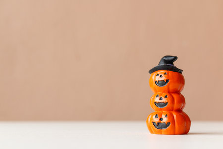 Stacked Halloween pumpkin figurine with carved faces and a witch hat on top on neutral background.の写真素材