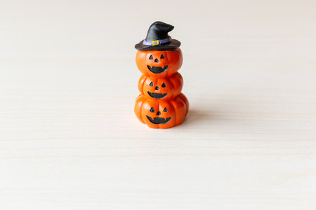 Stacked Halloween pumpkin figurine with carved faces and a witch hat on top on neutral background.の写真素材